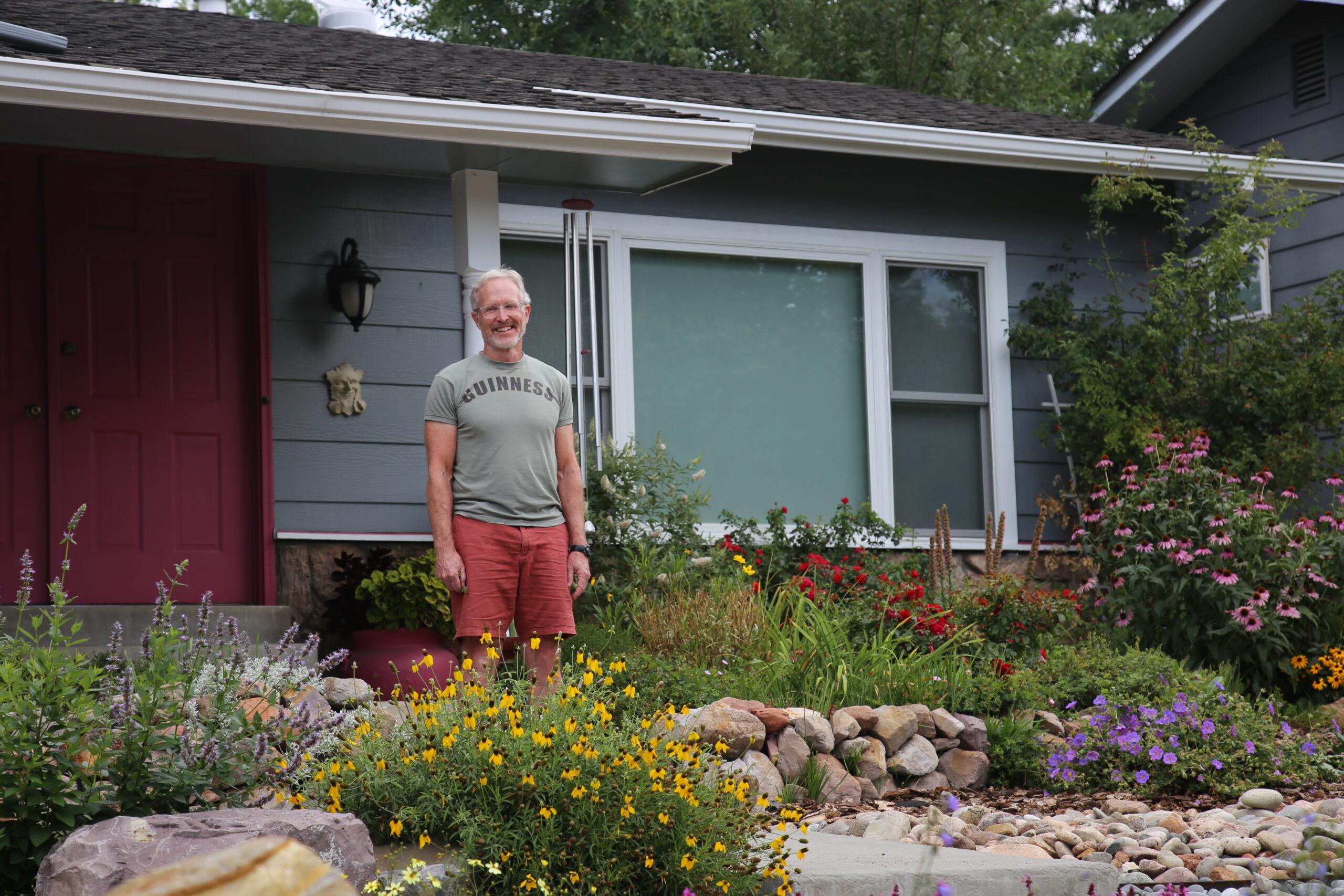 A man posing in his front yard full of low-water gardens.